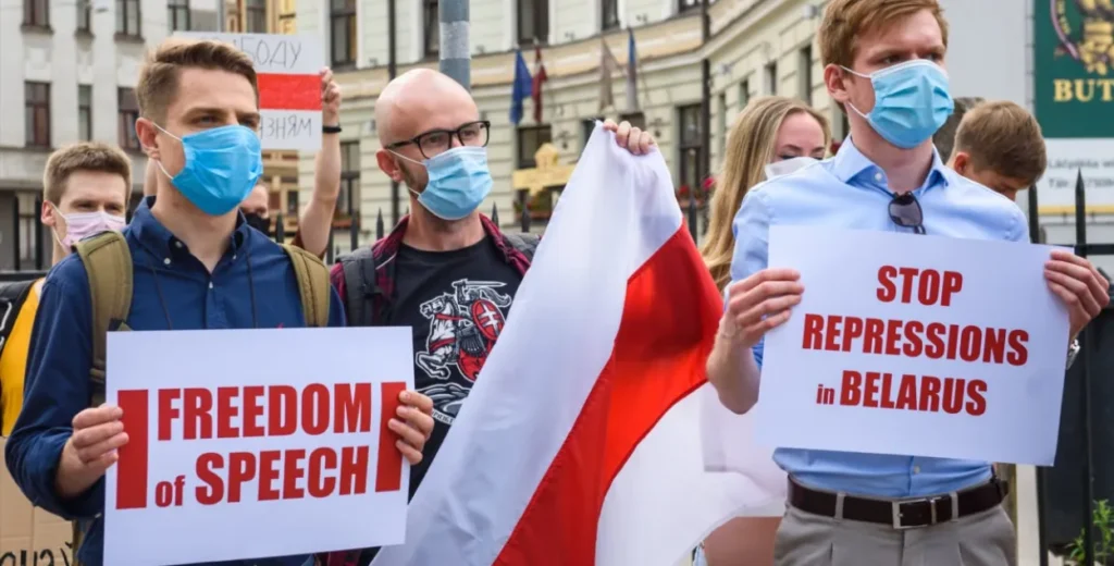 Belarus youth movements activists holding protest signs reading 'Freedom of Speech' and 'Stop Repressions in Belarus' while wearing face masks and carrying the historic white-red-white flag during a demonstration.