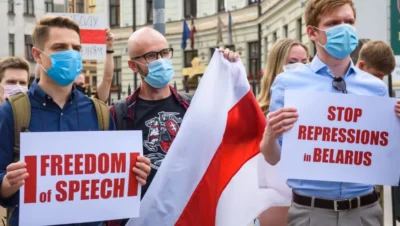 Belarus youth movements activists holding protest signs reading 'Freedom of Speech' and 'Stop Repressions in Belarus' while wearing face masks and carrying the historic white-red-white flag during a demonstration.