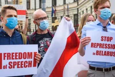 Belarus youth movements activists holding protest signs reading 'Freedom of Speech' and 'Stop Repressions in Belarus' while wearing face masks and carrying the historic white-red-white flag during a demonstration.