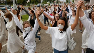 Women in Belarus 2025 marching in peaceful protest, wearing white clothing and face masks, holding hands as a symbol of unity and resistance against state repression.